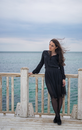 brunette girl in a black dress posing on the pierの写真素材