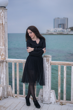 brunette girl in a black dress posing on the pierの写真素材