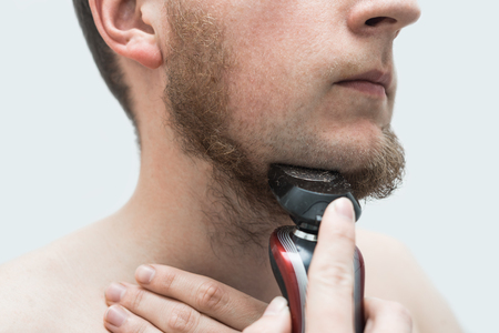 young man shaving his beard off with an electric shaverの写真素材