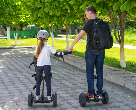 Young father and daughter riding electric mini hoverboard in park