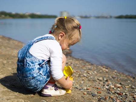 cute little girl play with sand and shovel on beach. She sits near waterの写真素材