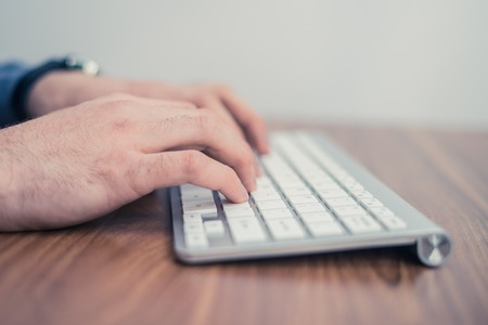 Hands typing on wireless keyboard on wooden table