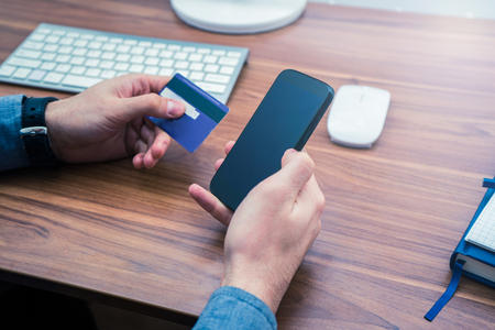 hands holding credit card and a typing on the phone making online purchase