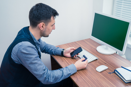 Office worker holding credit card and a typing on the phone making purchaseの写真素材