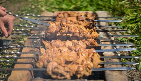 Mans hand turn over kebabs or barbecue on a grill of bricks. Travel conceptの写真素材