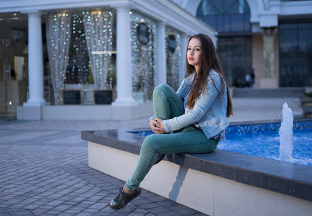 Alone beautiful girl sitting near fountain and looking on night cityの写真素材
