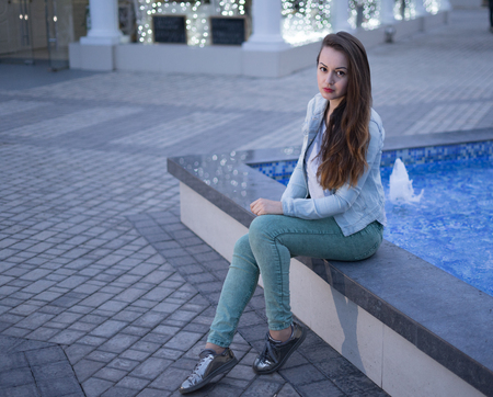 Alone beautiful girl sitting near fountain at night and looking at the camera.の写真素材