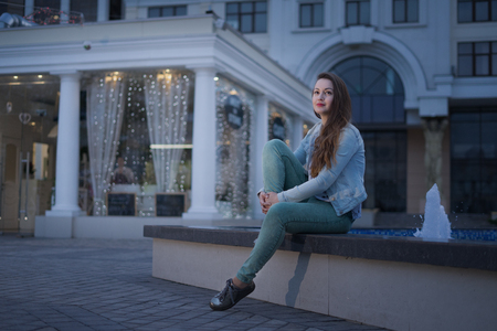Alone beautiful girl sitting near fountain and looking on night cityの写真素材