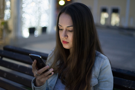 woman using smartphone sitting on the bench in night cityの写真素材