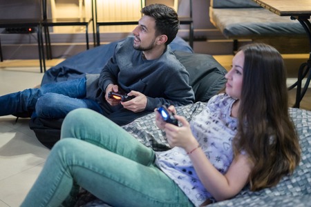 happy couple friends playing video games with joystick sitting on Bean bag chairの写真素材