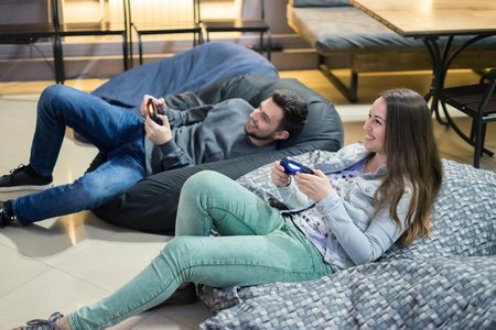 happy couple friends playing video games with joystick sitting on Bean bag chairの写真素材