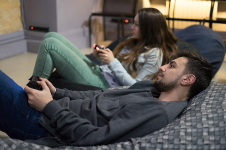 happy couple friends playing video games with joystick sitting on Bean bag chairの写真素材