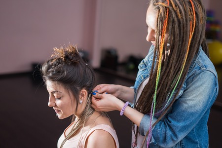 A hair stylist braids Zizi cornrows to a young and beautiful girlの写真素材