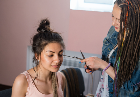 A hair stylist cuts Zizi cornrows from young and beautiful girl. new hairstyle without dreadlocks...