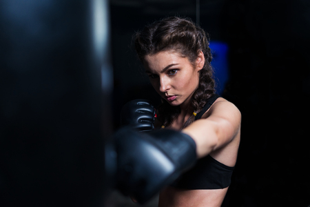 Young fighter boxer girl in training with heavy punching bagの写真素材