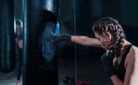 Young fighter boxer fit girl beating punching bag in gym. Womanの写真素材