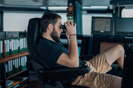 Deck navigation officer on the navigation bridge. He looks through binocularsの写真素材