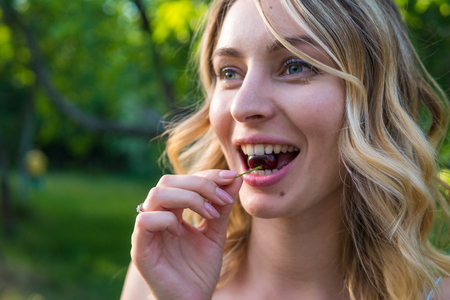 Girl eating cherries in outdoor park.の写真素材