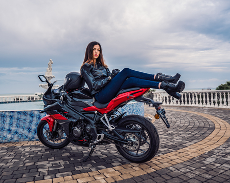 Biker girl in a leather jacket on a black and red color motorcycleの写真素材