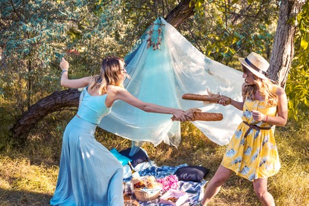 Playful girls fighting with bread baguette making picnicの写真素材