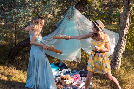 Playful girls fighting with bread baguette making picnicの写真素材