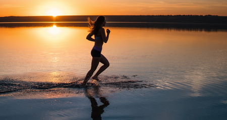 Woman Running on the Beach at Sunsetの写真素材