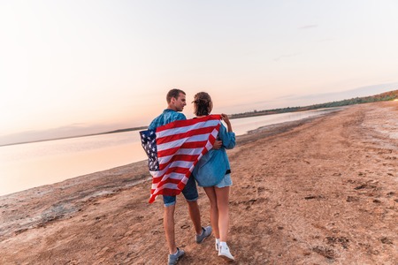 american couple covered in american flag walking on beachの写真素材