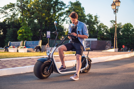 Handsome young man sitting on electric bike or scooterの写真素材