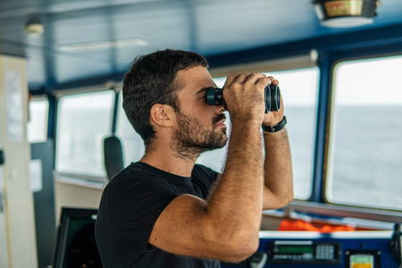 Navigational officer lookout on navigation watch looking through binocularsの写真素材