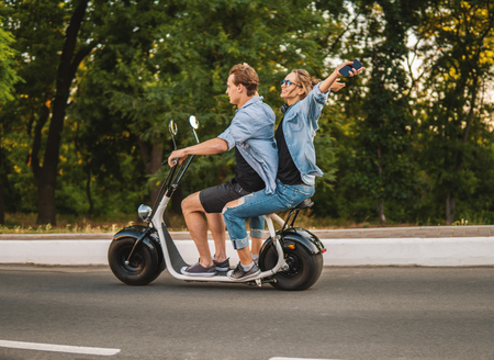 Lovely young couple driving electric bike during summerの写真素材