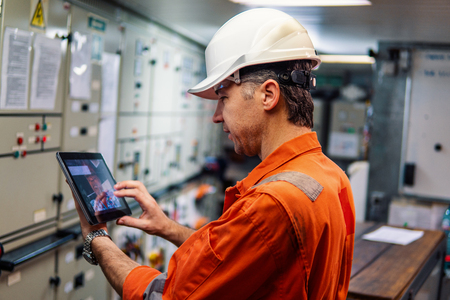 Marine chief engineer watching digital tablet in engine control room