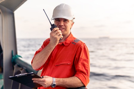 Deck Officer on deck of offshore vessel holds VHF walkie-talkie radioの写真素材