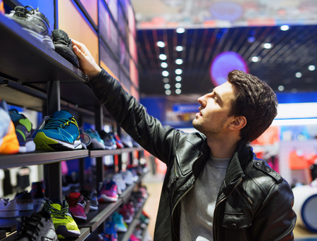 young male customer choosing sneakers at supermarket storeの写真素材