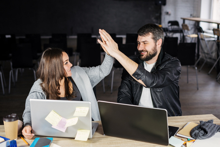 Smiling  couple using laptops and giving high fiveの写真素材