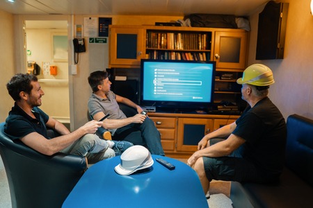 Happy team of ship officers watch TV onboard of vesselの写真素材