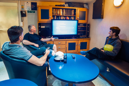 Happy team of ship officers watch TV onboard of vesselの写真素材