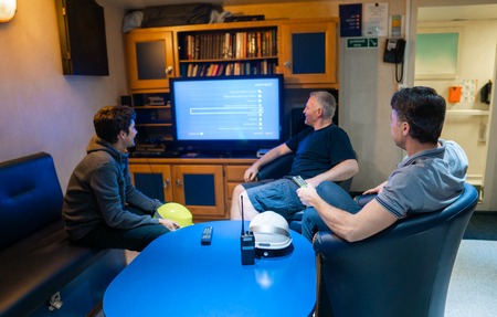 Happy team of ship officers watch TV onboard of vesselの写真素材