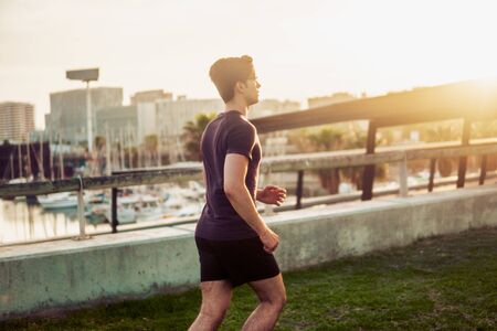 Young athletic man running at park with skyscrapers background