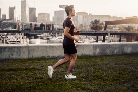Young athletic man running at park with skyscrapers backgroundの写真素材