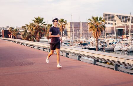 Young athletic man running at park during skyscrapers backgroundの写真素材