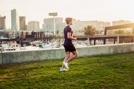 Young athletic man running at park with skyscrapers backgroundの写真素材
