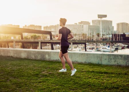 Young athletic man running at park with skyscrapers backgroundの写真素材