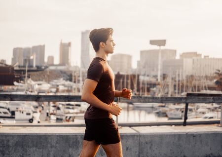 Young athletic man running at park with skyscrapers backgroundの写真素材