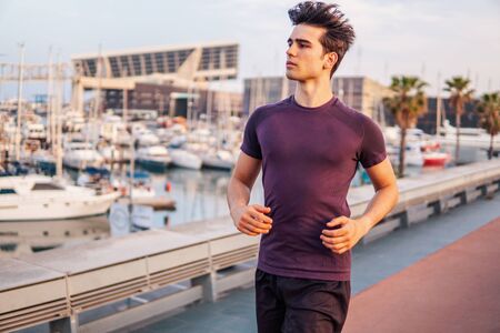 Young athletic man running at park during skyscrapers backgroundの写真素材