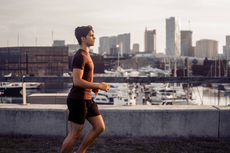 Young athletic man running at park with skyscrapers backgroundの写真素材