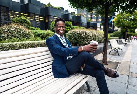 African American businessman wearing blue suit drinks coffee near officeの写真素材