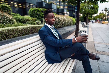 African American businessman wearing blue suit drinks coffee near officeの写真素材