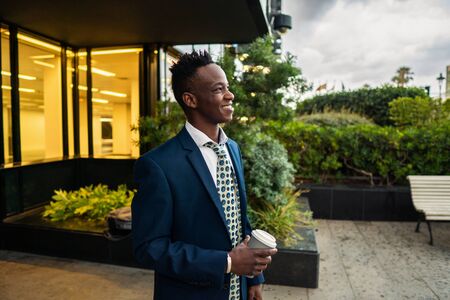 African American businessman wearing blue suit drinks coffee near officeの写真素材