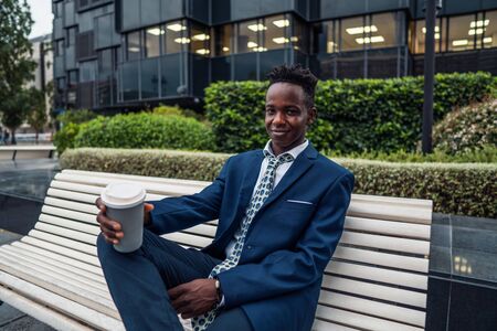 African American businessman wearing blue suit drinks coffee near officeの写真素材