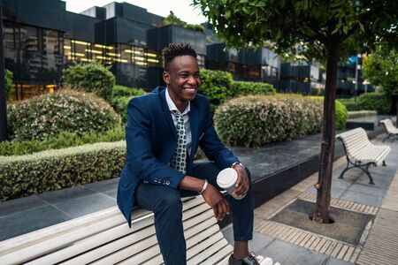 African American businessman wearing blue suit drinks coffee near officeの写真素材